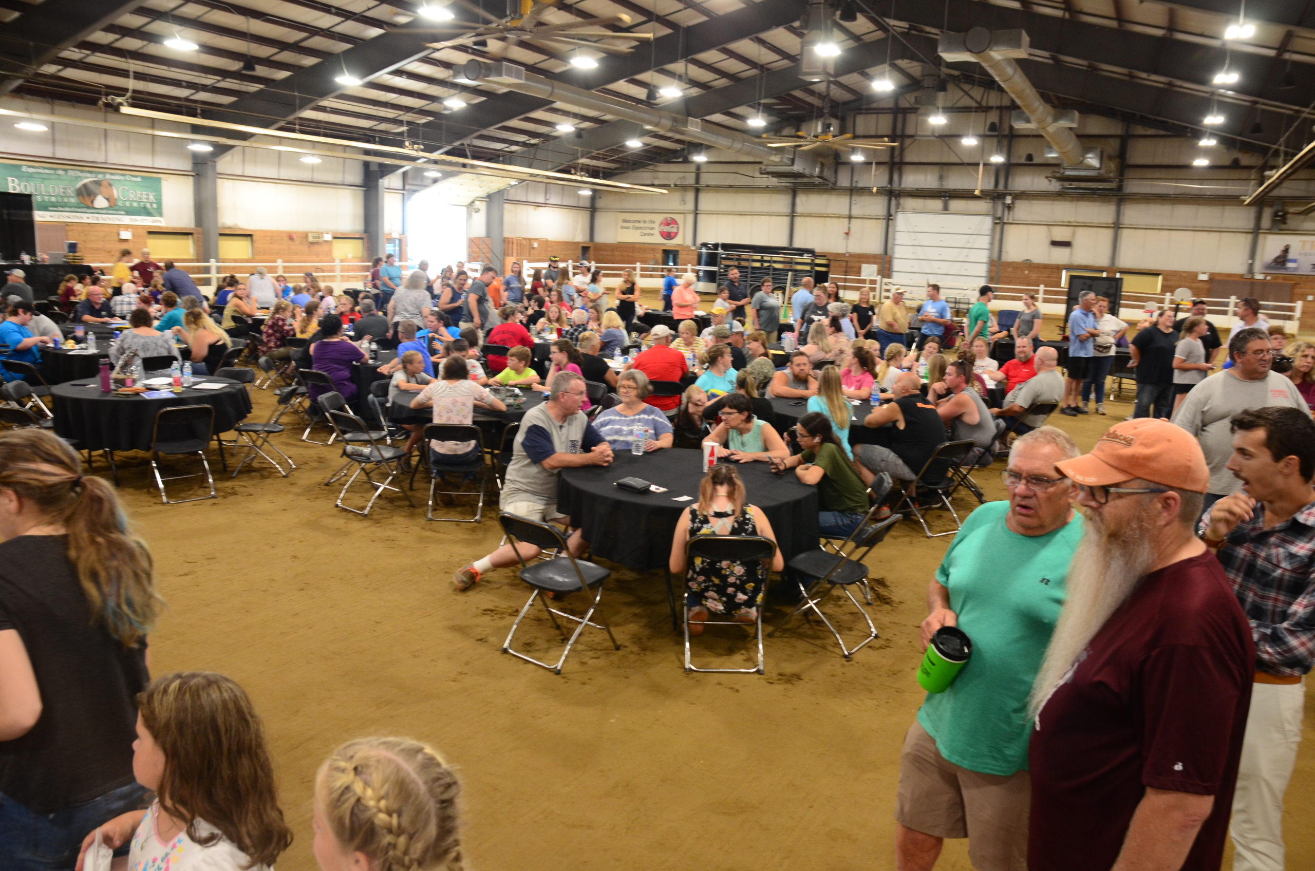 Large indoor gathering with people seated at tables and socializing.