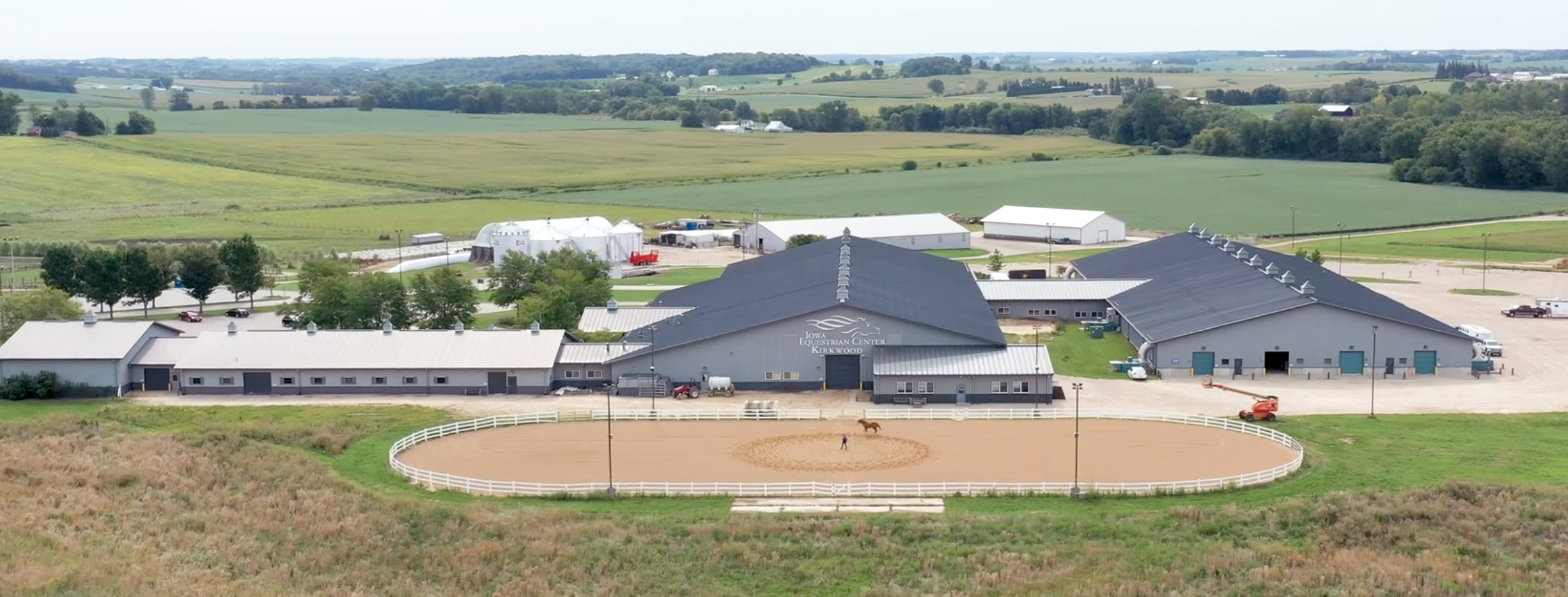 A large equestrian arena and stable complex set in a rural landscape.